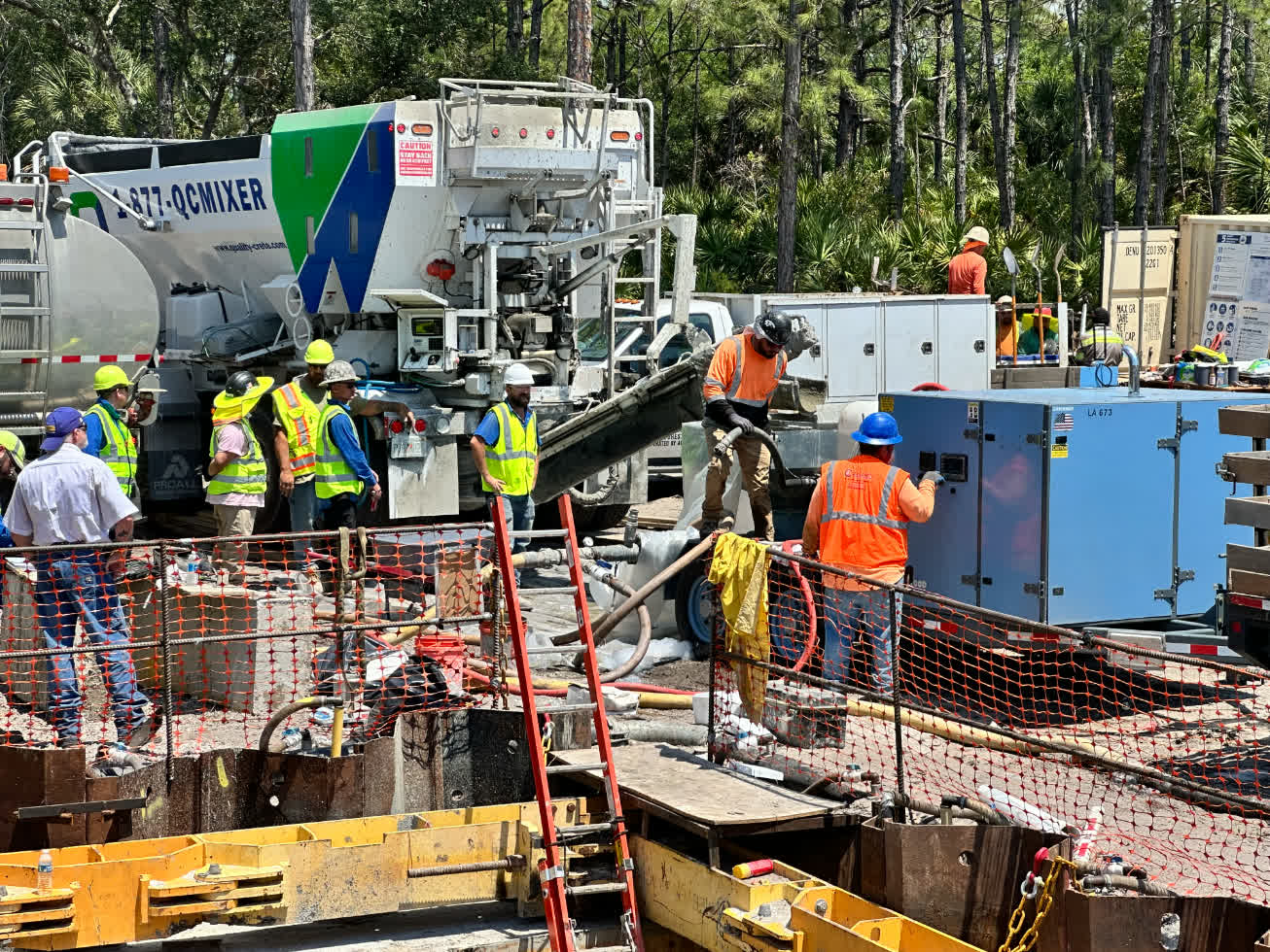 Crew placing concrete from a Quality-Crete volumetric mixer beside a shored trench