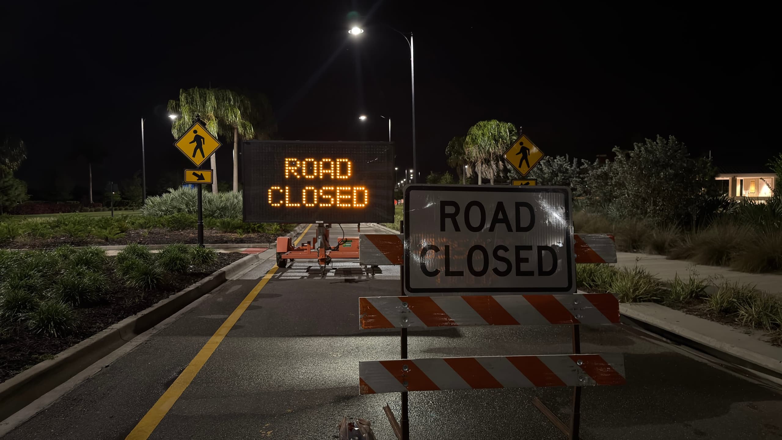 Road-closed barricades and a lit warning sign across an empty street at night