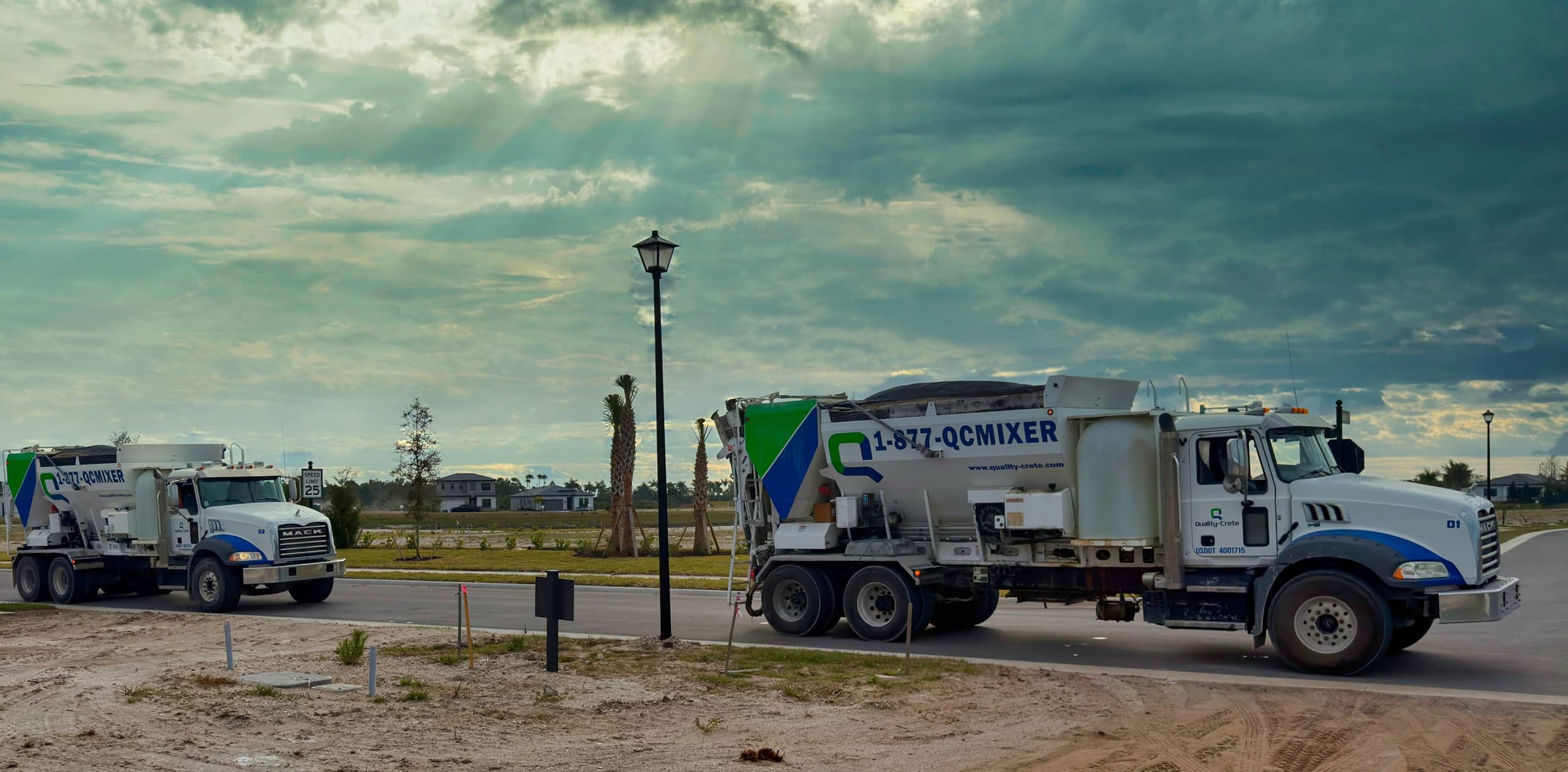 Two Quality-Crete mixer trucks on a jobsite road under a dramatic sky