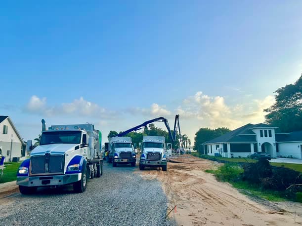 Quality-Crete mixer and boom pump trucks staged on a residential street at dawn, boom extended over the jobsite