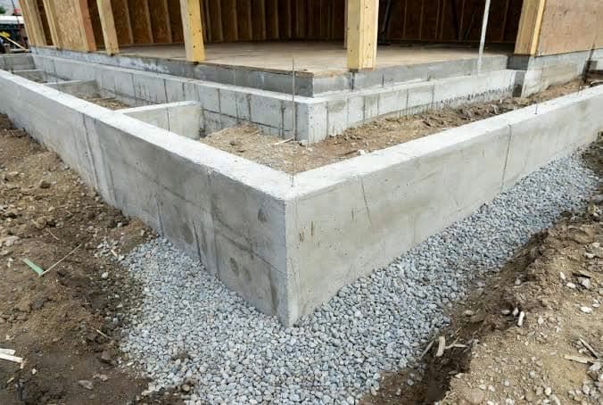 Poured concrete stem-wall foundation with gravel backfill beneath a house frame