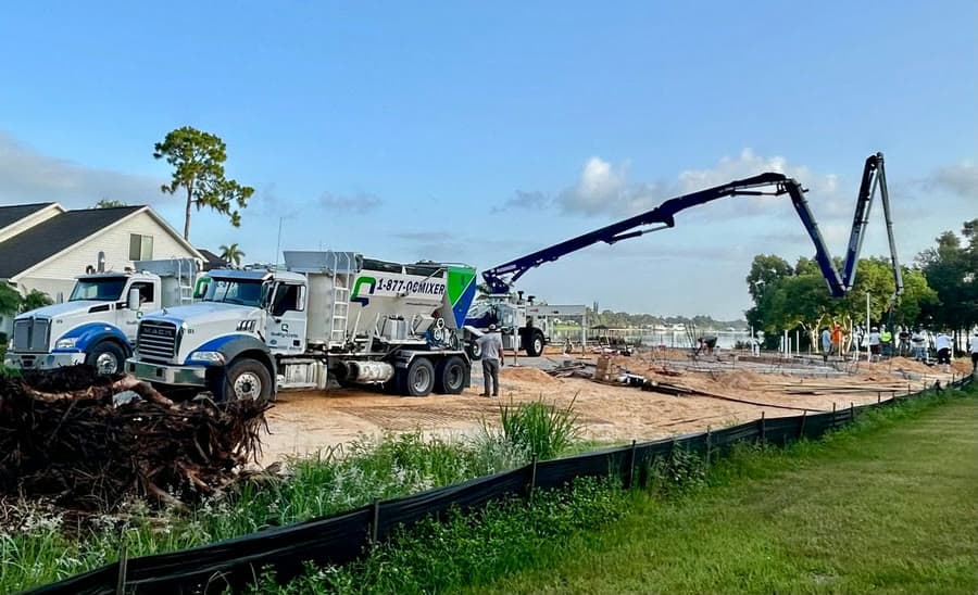 Quality-Crete mixer trucks feeding a concrete pump boom at a residential waterfront jobsite