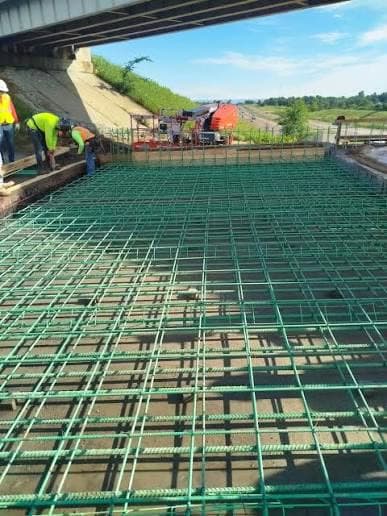 Rebar mat prepared for a bridge approach slab pour, with a concrete mixer staged nearby
