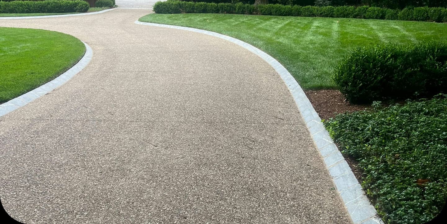 Curved pervious concrete driveway bordered by lawn and hedges