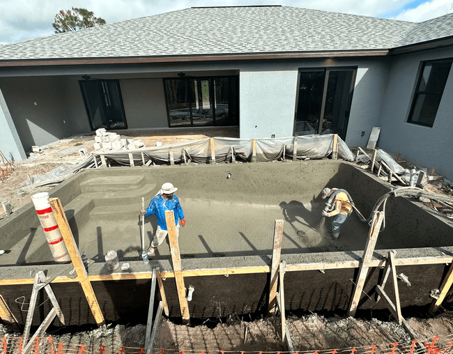 Freshly placed shotcrete pool shell in a backyard beside a modern home
