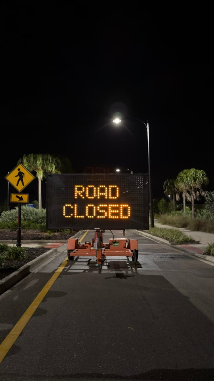Illuminated "Road Closed" sign blocking a travel lane near a pedestrian crossing at night